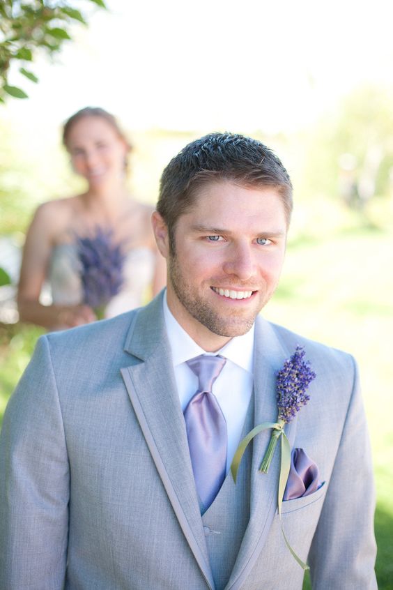 the groom wearing a light grey suit with a lavender tie and a lavender boutonniere