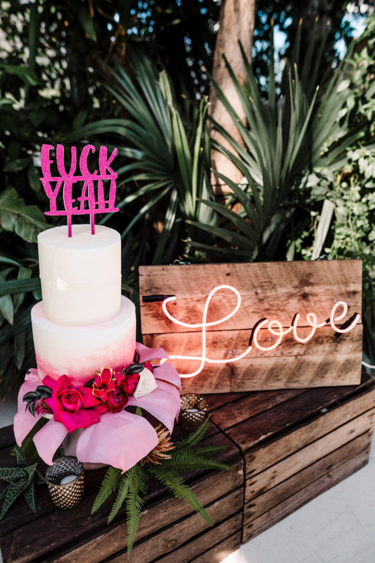 A pink palm leaf for displaying the wedidng cake, a fun cake topper and a neon sign added glam and fun