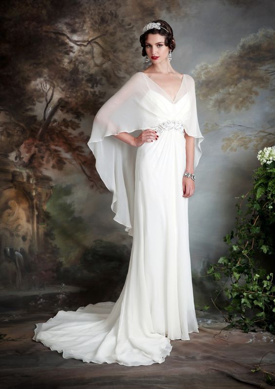 an ivory wedding dress with spaghetti straps and a ruffled cape attached to the embellished belt