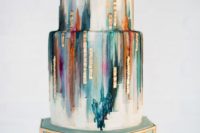 10 a wedding cake with colorful green, teal, orange, purple strokes, geometric gold decor and toppers
