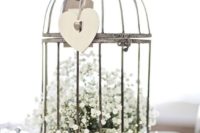 12 a metal cage on legs with baby’s breath inside and a cutout heart hanging outside