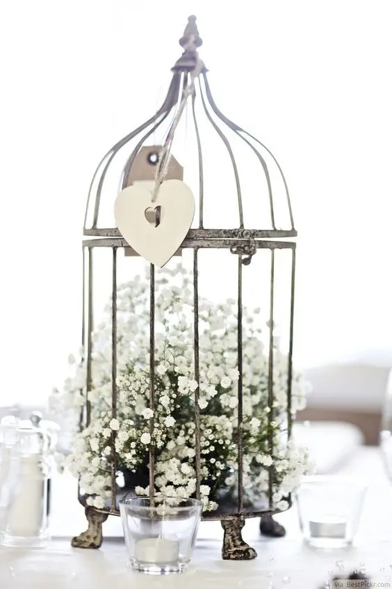 a metal cage on legs with baby's breath inside and a cutout heart hanging outside