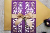 12 a purple laser cut invitation with a vintage key attached and a gold envelope