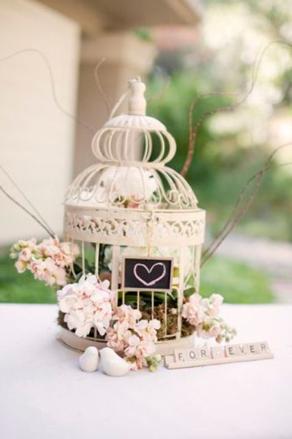 a small cage with a chalkboard sign, pink blooms and greenery