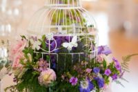 15 a white birdcage with lush foliage, purple and pink blooms for a colorful big day
