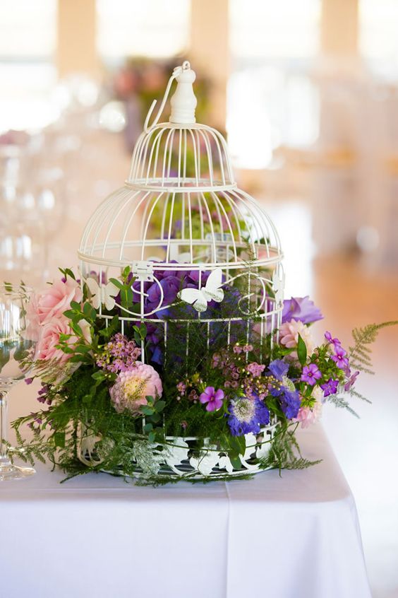a white birdcage with lush foliage, purple and pink blooms for a colorful big day