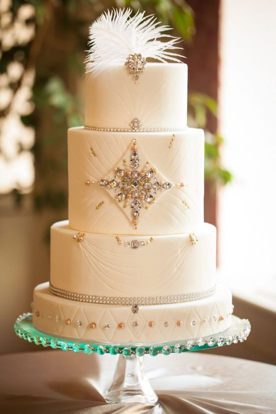 a gorgeous white wedding cake with beads, rhinestones and a feather on top