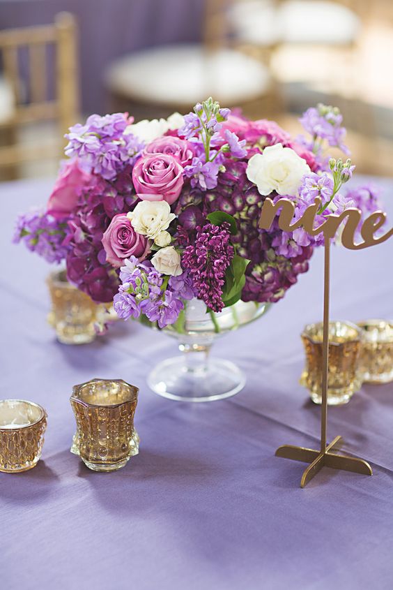 a lush floral centerpiece in the shades of lilac, purple and cream and gold candle holders