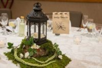 16 a wedding centerpiece of moss, neutral blooms, a candle lantern and the name of the table