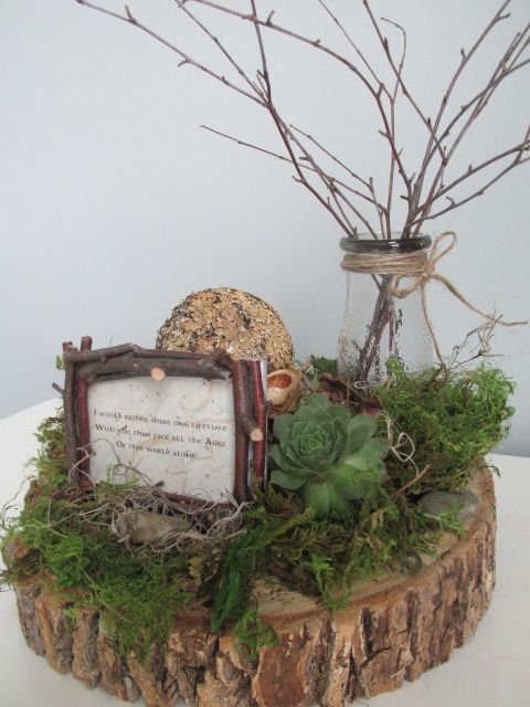 a wood slice with moss and a succulent, stone, a vase with branches and a framed quote for a centerpiece