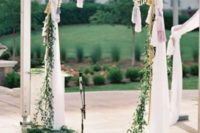a wedding arch with flowing draperies, greenery, pompom trim and tassels
