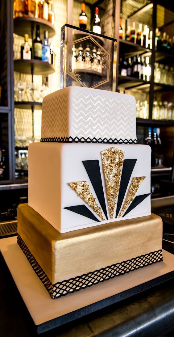 a chic square cake with a gold layer, a white layer decorated with black and gold glitter triangles and a gold and white chevron layer