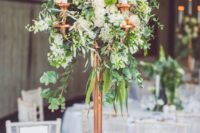22 a tall copper candle stand with lush greenery and neutral flowers as a stunning centerpiece
