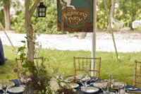 22 the table decorated in navy and green, with a branch centerpiece, a lantern and a sign with the name of the tavern