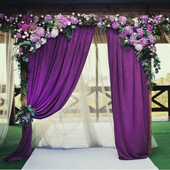 a wedding arch with purple curtains, hydrangeas and greenery