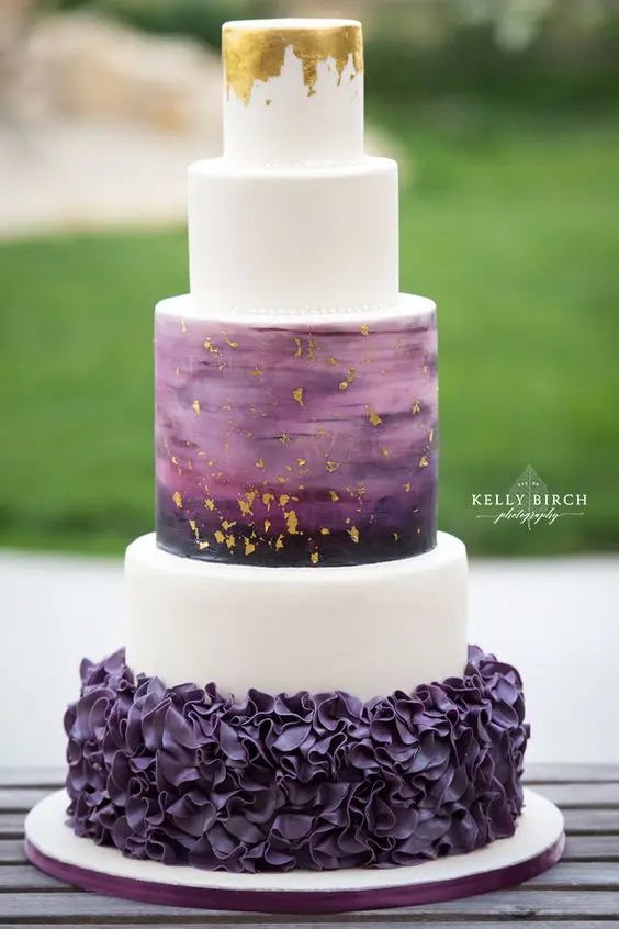 a unique modern wedding cake with a purple ruffle layer, white layers, an ombre purple gold leaf layer and a gold leaf top layer