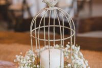 27 a small vintage cage with a bird on top placed on a wooden slice, a candle and baby’s breath
