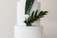 28 an exquisite white wedding cake decorated with tropical leaves and a single white bloom
