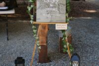 LOTR wedding decor with a grey sign with vines, candle lanterns, tree slices and white petals is a cool idea