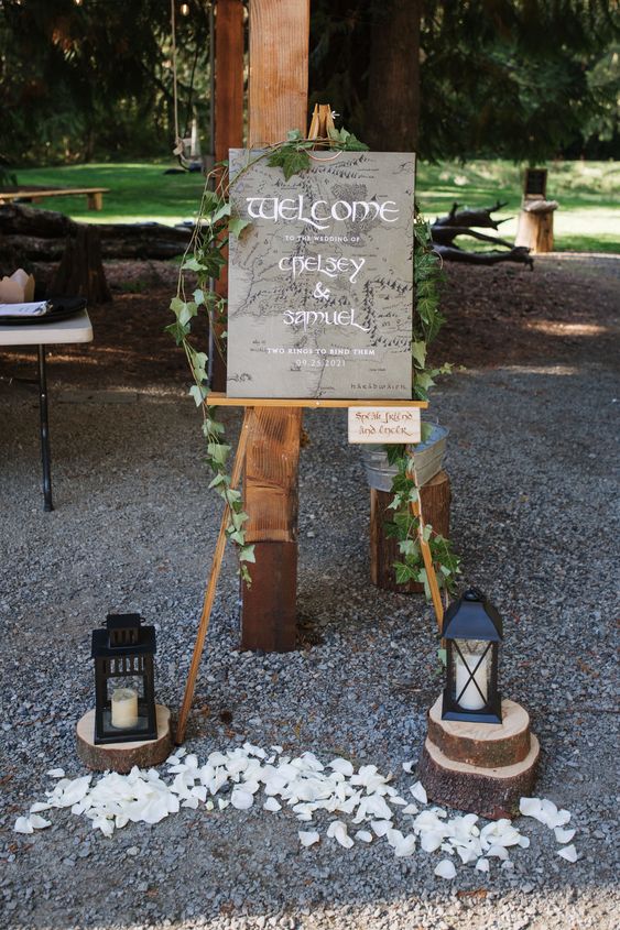 LOTR wedding decor with a grey sign with vines, candle lanterns, tree slices and white petals is a cool idea