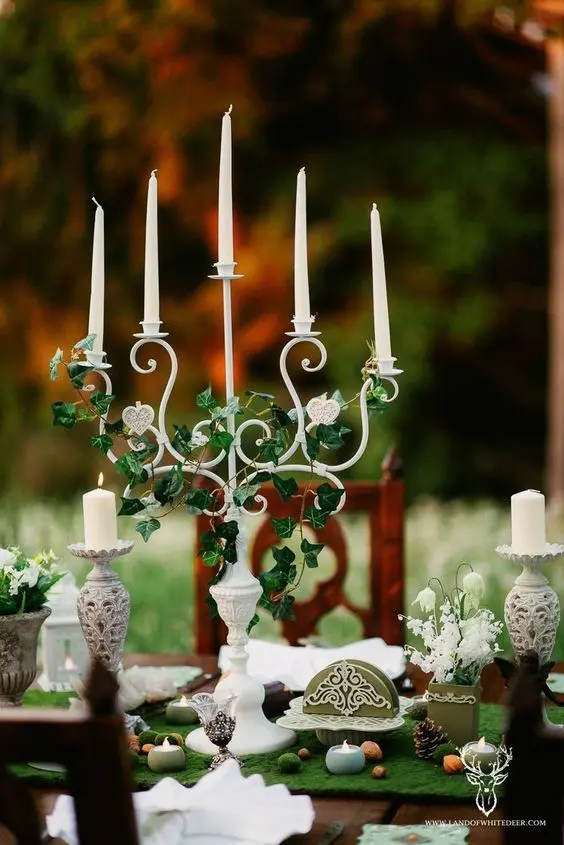 a LOTR wedding centerpiece of a candelabra with vines, white blooms, pinecones, nuts and candles is creative