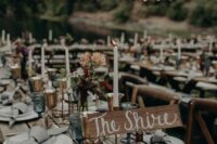 a LOTR wedding reception outdoors, with lights over the space, wooden tables and benches, greenery and blooms and candles