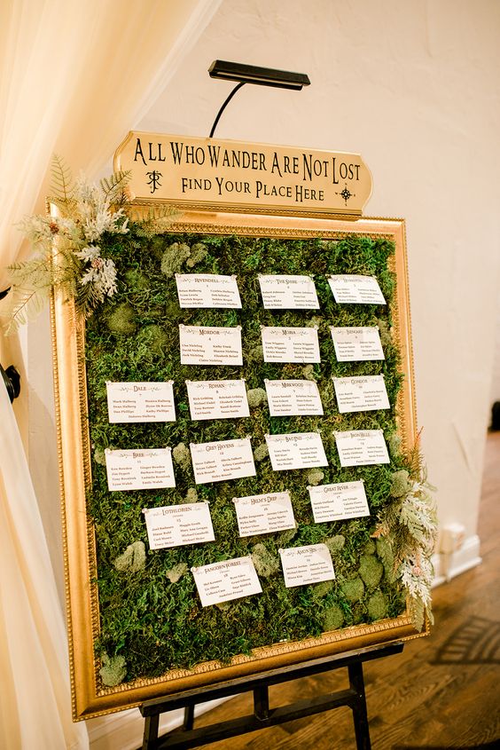 a LOTR wedding seating chart covered with moss and greenery, with cards and a sign on top is a cool idea