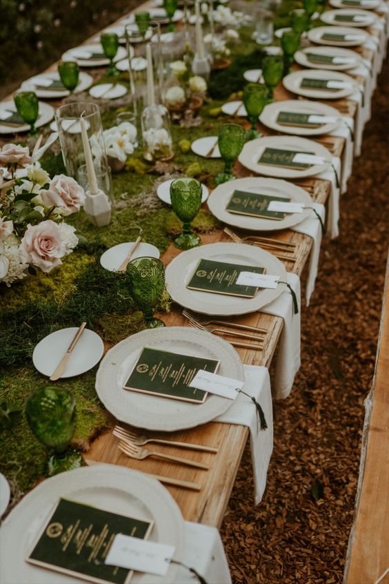 a LOTR wedding tablescape with a moss runner, greenery, blush roses, green glasses and green menus plus gold cutlery