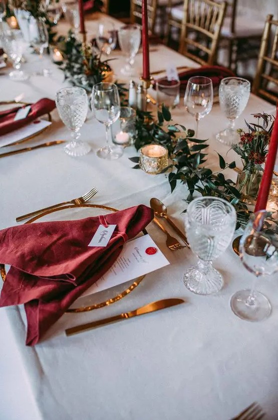 a beautiful Christmas wedding tablescape with a greenery table runner, red candles and red napkins, gold rimmed plates