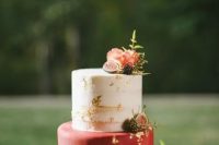 a beautiful and chic wedding cake with a naked and a red tier with gold leaf, with pink blooms, berries and a bit of greenery is a refined idea for a fall wedding