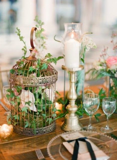 a beautiful garden wedding centerpiece of a brass cage with blush roses and greenery and a candle in a candleholder