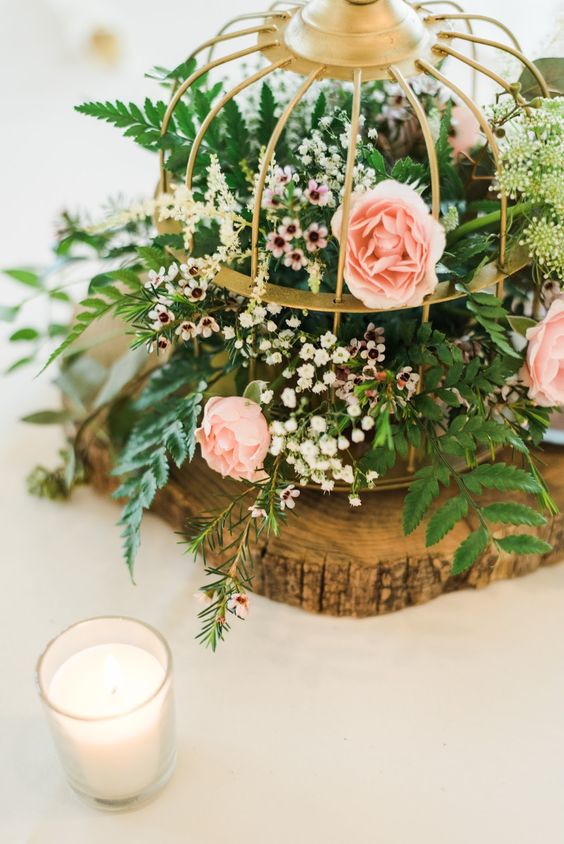a beautiful spring wedding centerpiece of a tree slice, a cage with waxflower, pink blooms and greenery is wow