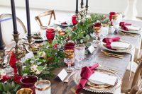 a beautiful wedding tablescape with a greenery and red rose runner, black candles, red glasses and napkins