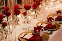 a beautiful wedding tablescape with white linens, red roses and tall and thin candles, gold chargers and cutlery