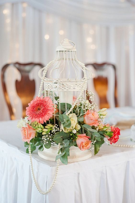 a beautiful white cage with coral, pink and yellow blooms, greenery and baby's breath is amazing