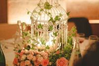 a birdcage surrounded with pink blooms and greenery and with candles inside is a lovely and romantic centerpiece