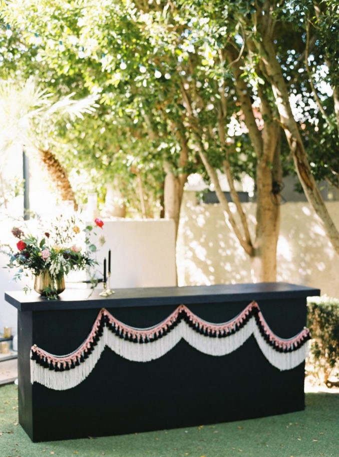a black wedding bar stand with white fringe and pink and black tassels for decor, black candles and bold blooms and greenery