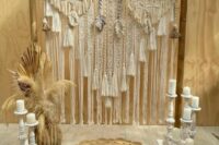 a boho wedding backdrop with macrame, tassels, pampas grass, fronds and pillar candles plus a woven rug is a cool idea for a boho neutral wedding