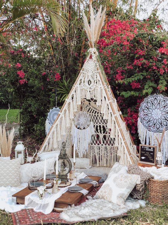 a boho wedding lounge with a macrame teepee with tassels, a low table with lovely place settings and candles
