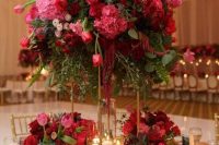 a bold and catchy wedding tablescape with lush red and pink floral arrangements and greenery , gold chargers and cutlery