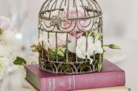 a book stack with a shabby chic cage, blush and white blooms and greenery is a chic vintage wedding idea