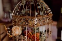 a brass birdcage with yellow and burnt orange blooms and greeneyr is a lovely fall wedding decor idea