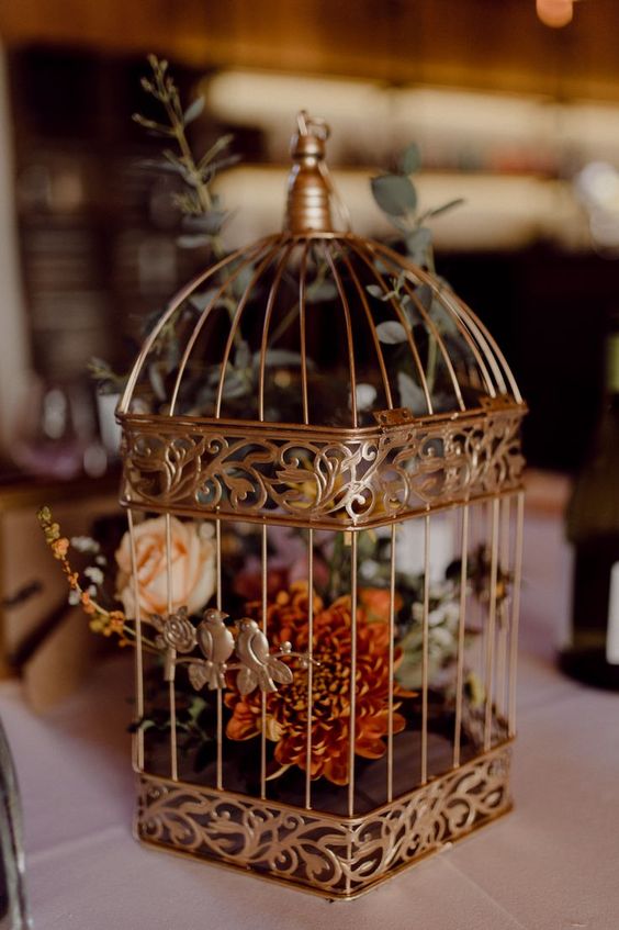 a brass birdcage with yellow and burnt orange blooms and greeneyr is a lovely fall wedding decor idea