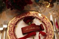 a bright wedding tablescape with a bold floral arrangement, a red and gold plate and rose, gold cutlery is wow