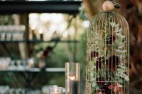 a cage with burgundy and white blooms and greenery and grey pillar candles is a chic idea for the fall