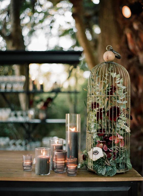 a cage with burgundy and white blooms and greenery and grey pillar candles is a chic idea for the fall