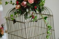 a cage with petals, pink blooms, berries and greenery on top is a creative wedding centerpiece