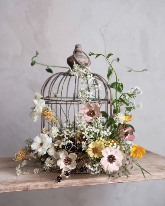 a cage with white, blush and yellow blooms, berries and greenery is a refined garden wedding idea
