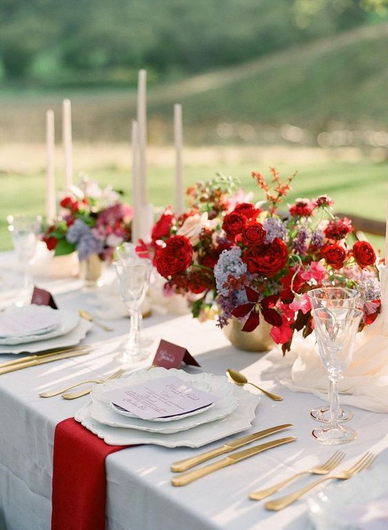 a catchy and bold red and gold wedding tablescape with lush red floral arrangements, red napkins, white porcelain and gold cutlery