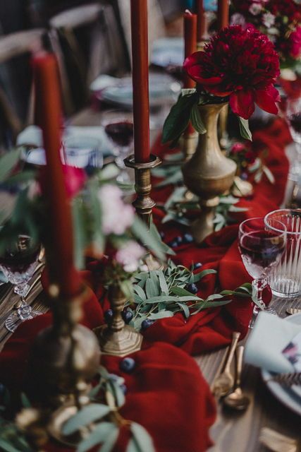 a catchy red and gold wedding tablescape with a red table runner, red blooms and candles, gold vases and candleholders